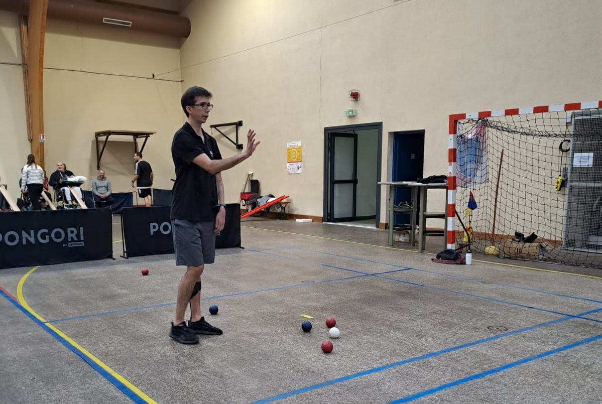 Personne debout dans un gymnase avec des boules de boccia parterre à côté de lui