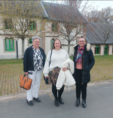Trois femmes se tiennent ensemble à l’extérieur, devant une maison, en posant pour une photo.